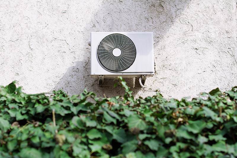 horizontal front view of a white air conditioning unit behind a decorative garden wall of green leaves