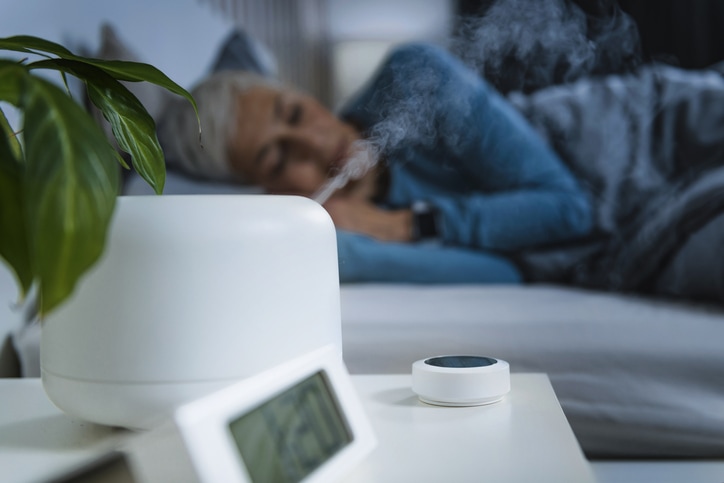 Air Humidifier increasing the humidity in a bedroom for better sleep. Beautiful mature woman sleeping in bed.
